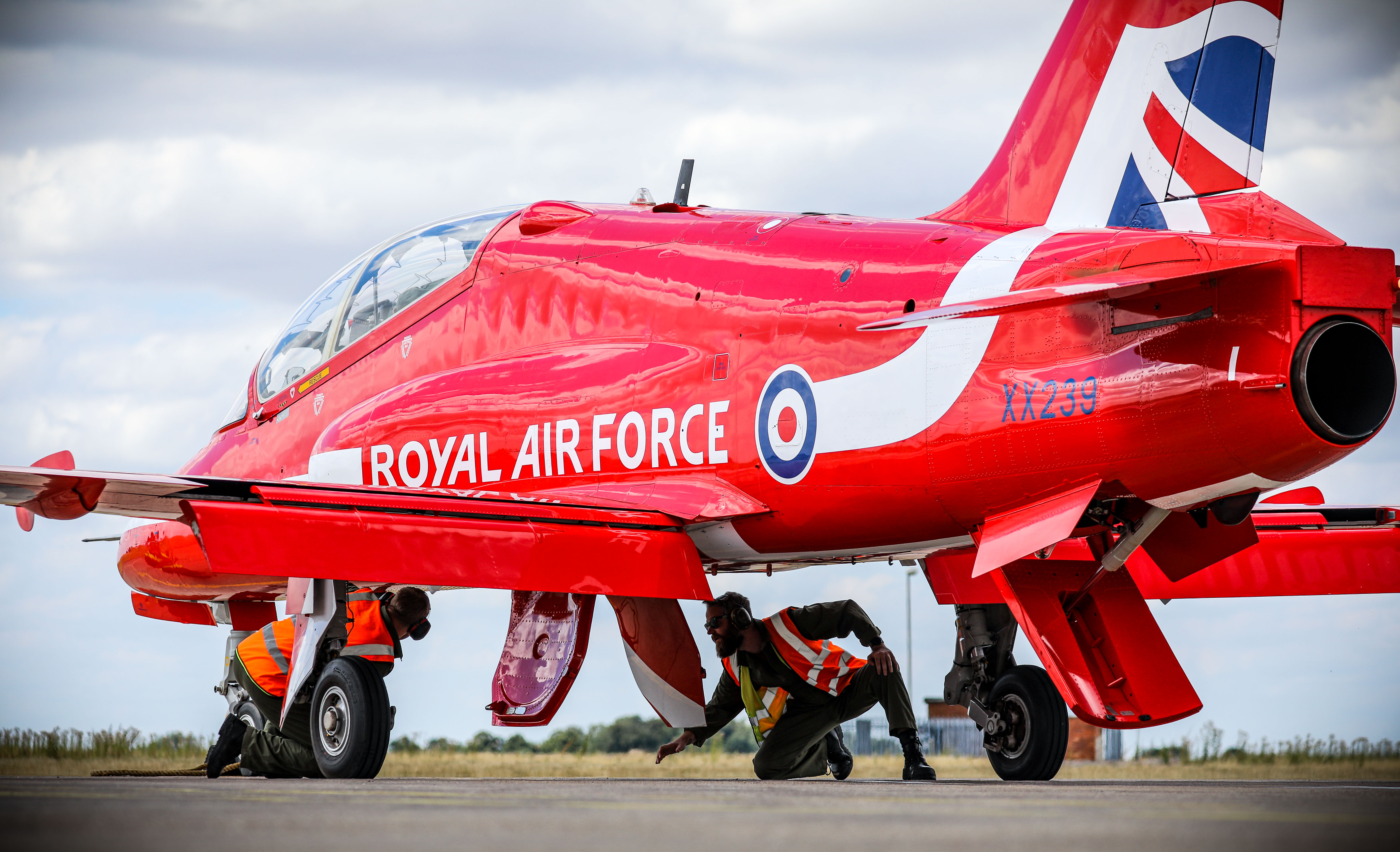 Image shows RAF Pilot underneath a Red Arrow Hawk aircraft.